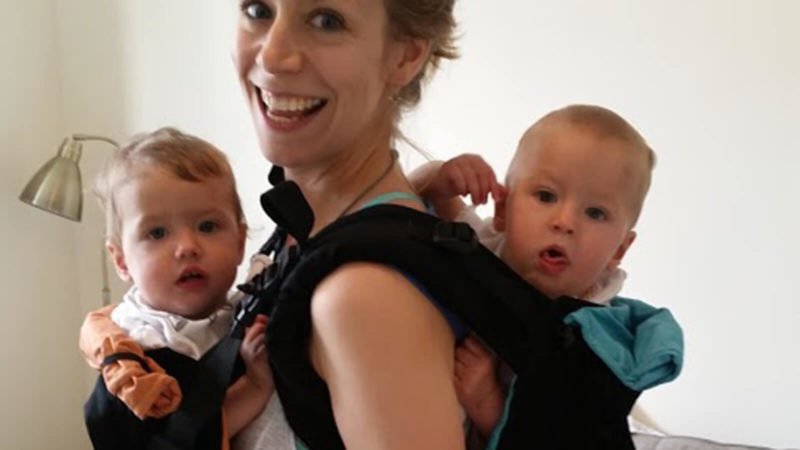 Woman carries one baby on her front and one on her back in the TwinGo twin baby carrier