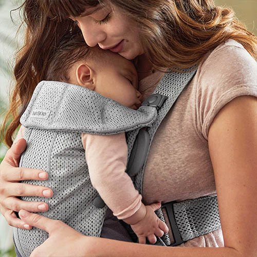 Woman carries baby facing towards her chest in the BabyBjorn Baby Carrier Mini in Grey mesh, side view