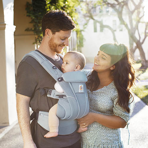 Man carries baby in Ergobaby Omni Breeze carrier while woman smiles with them