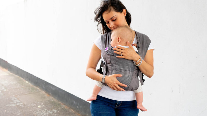 Woman carries baby facing towards her in grey Izmi Breeze Baby Carrier