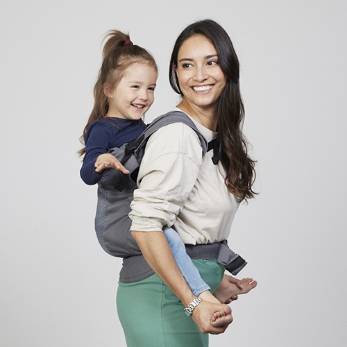 Woman carries toddler on her back in Izmi Breeze Toddler Carrier