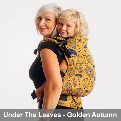 Woman carries toddler on her back in Lenny Lamb Preschool carrier in yellow Under the Leaves - Golden Autumn fabric, side view