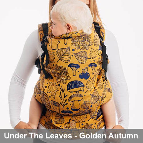 Woman carries toddler on her front in Lenny Lamb Preschool carrier in yellow Under the Leaves - Golden Autumn fabric