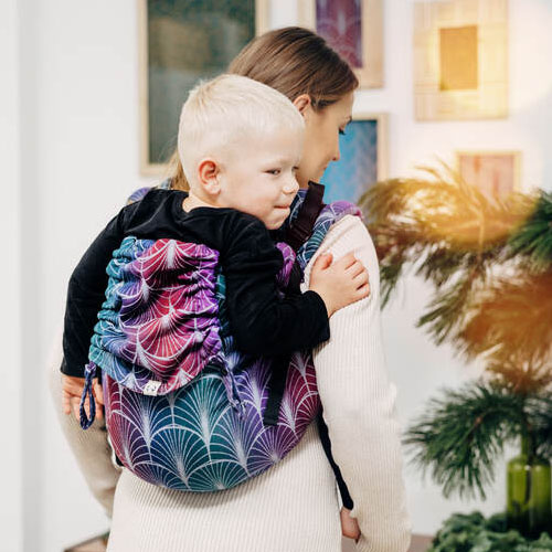 Woman carries child on her back in Lenny Lamb Buckle Onbuhimo Preschool carrier in Deco Kingdom, back view