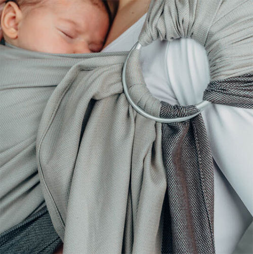 Woman carries baby on her front in Lenny Lamb Ring Sling in Cool Grey fabric