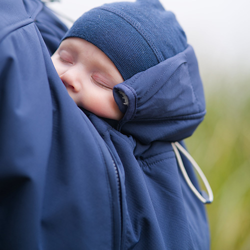 Close up of sleeping baby being carried by woman wearing the Mamalila Cosy Allrounder babywearing coat in Navy