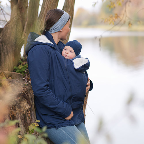 Woman carries baby on her front while wearing the Mamalila Cosy Allrounder babywearing coat in Navy