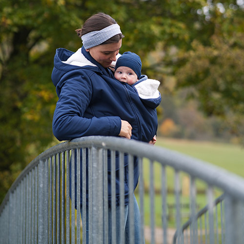 Woman carries baby on her front while wearing the Mamalila Cosy Allrounder babywearing coat in Navy