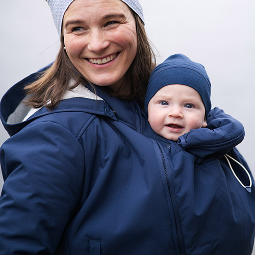 Woman carries baby on her front while wearing the Mamalila Cosy Allrounder babywearing coat in Navy