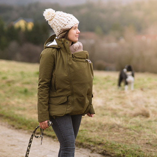 Woman carries baby in baby carrier while wearing Mamalila Cosy Allrounder allweather winter warm babywearing jacket