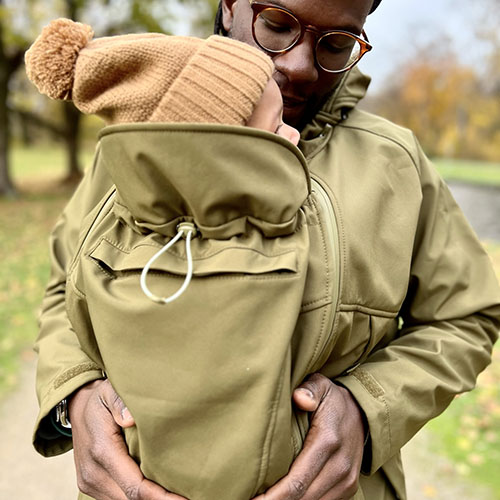 Man carries baby in carrier while wearing the Mamalila Mens Softshell Allrounder babywearing jacket in khaki