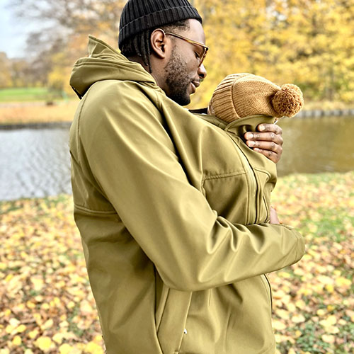 Man carries baby in carrier while wearing the Mamalila Mens Softshell Allrounder babywearing jacket in khaki