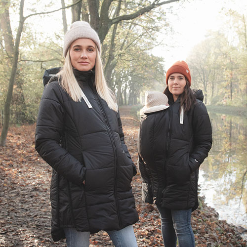 A pregnant woman and a woman carrying a baby in a carrier both wear the Mamalila Copenhagen babywearing coat in black