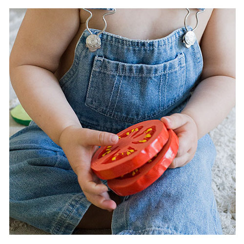 Toddler holds two tomato shaped rubber teething toy by Oli & Carol